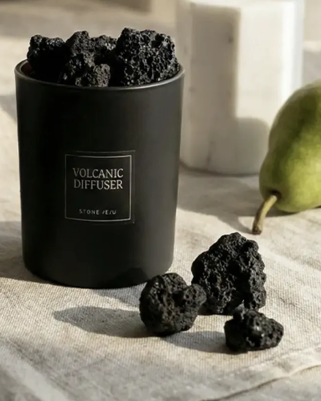 StoneJeju Volcanic Diffuser 350 in its black glass vessel, with loose pieces of scoria beside it